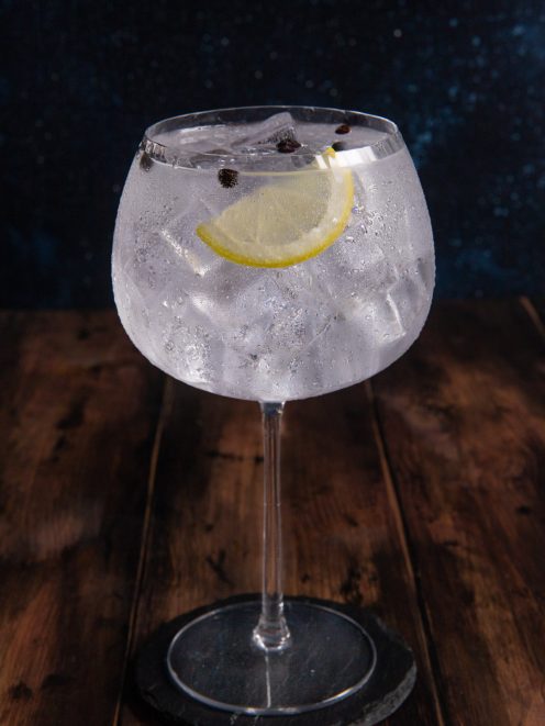 Gin tonic con ghiaccio abbondante, fetta di limone e bacche di ginepro