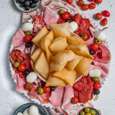 Gnocco fritto dorato al centro di un vassoio con salumi, mozzarelle, olive e pomodorini