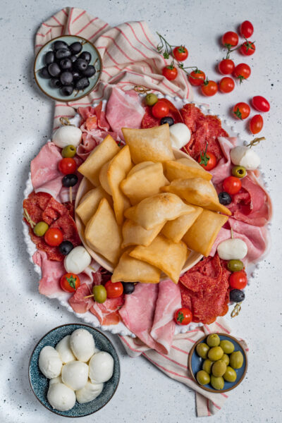 Gnocco fritto dorato al centro di un vassoio con salumi, mozzarelle, olive e pomodorini