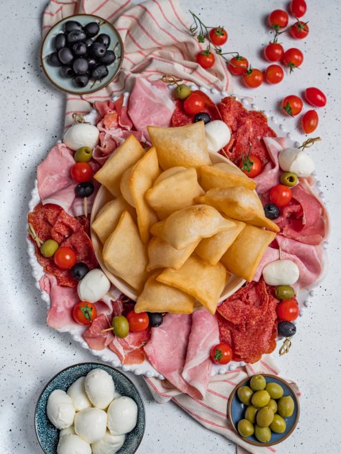 Gnocco fritto dorato al centro di un vassoio con salumi, mozzarelle, olive e pomodorini