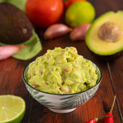 Guacamole cremoso con pezzi di avocado, servito con lime e peperoncini freschi