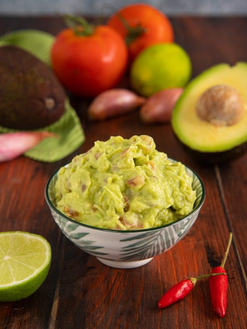 Guacamole cremoso con pezzi di avocado, servito con lime e peperoncini freschi