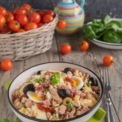 Insalata di riso con tonno, olive, prosciutto, uovo sodo, piselli e pomodori secchi