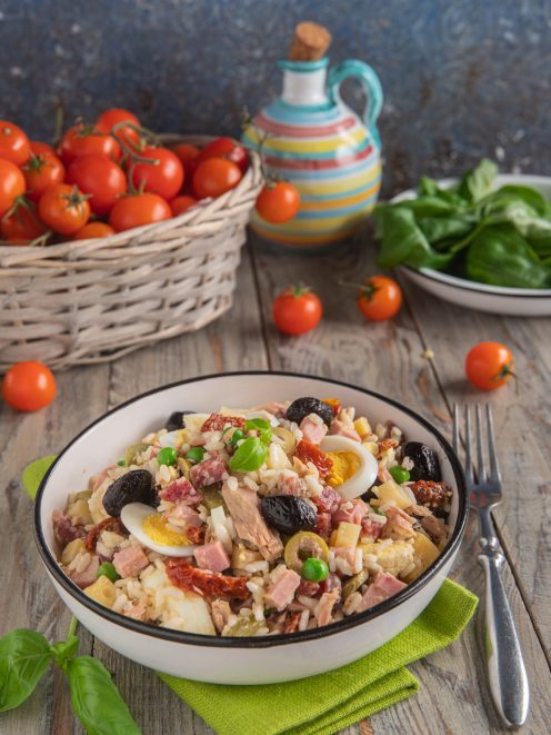 Insalata di riso con tonno, olive, prosciutto, uovo sodo, piselli e pomodori secchi