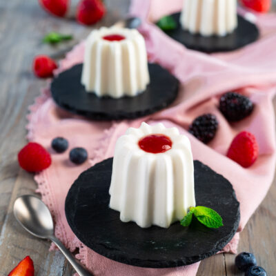 Panna cotta con coulis di fragole al centro, servita con frutti di bosco freschi e foglioline di menta