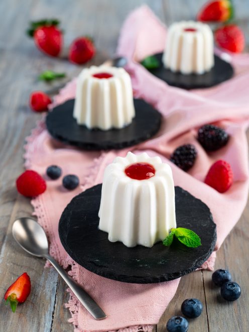 Panna cotta con coulis di fragole al centro, servita con frutti di bosco freschi e foglioline di menta
