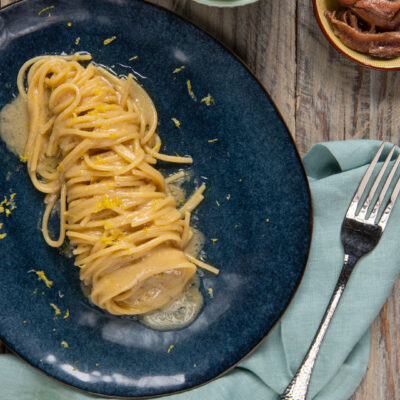 Pasta al burro, acciughe e limone arrotolata nel piatto con scorza grattugiata in superficie