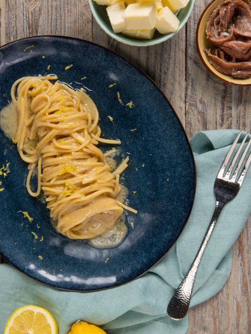 Pasta al burro, acciughe e limone arrotolata nel piatto con scorza grattugiata in superficie