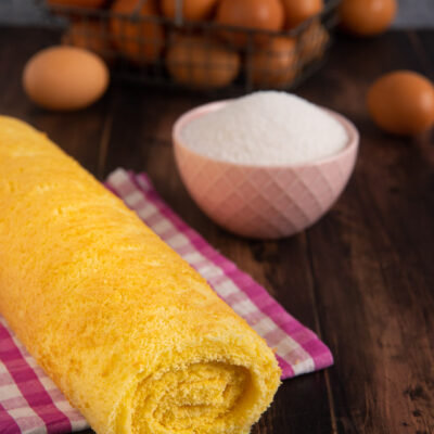 Pasta biscotto arrotolata a rotolo dorato e soffice su un canovaccio a quadretti