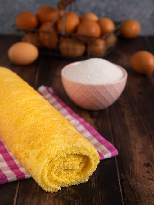 Pasta biscotto arrotolata a rotolo dorato e soffice su un canovaccio a quadretti