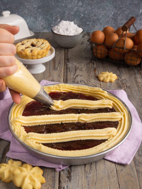 Pasta frolla montata spremuta con sac à poche su uno strato di confettura di frutti rossi