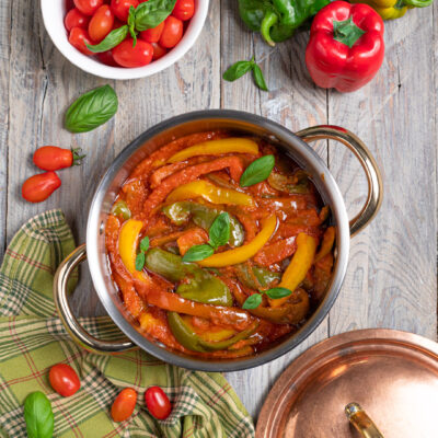 Peperonata con strisce di peperoni gialli e verdi in salsa di pomodoro, guarnita con foglie di basilico fresco