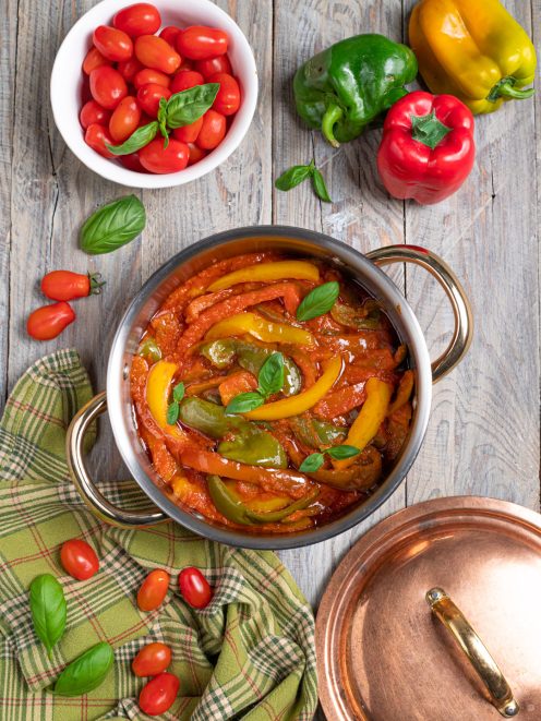 Peperonata con strisce di peperoni gialli e verdi in salsa di pomodoro, guarnita con foglie di basilico fresco