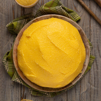 Polenta compatta servita nel tagliere di legno, con farina di mais a lato