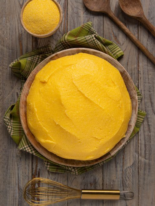 Polenta compatta servita nel tagliere di legno, con farina di mais a lato