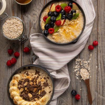 Due porridge con topping diversi: frutti di bosco e miele il primo, banana cioccolato e mandorle il secondo