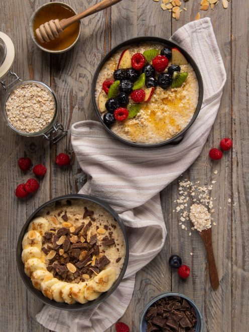 Due porridge con topping diversi: frutti di bosco e miele il primo, banana cioccolato e mandorle il secondo