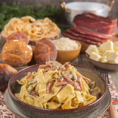 Tagliatelle con speck e funghi condite con prezzemolo tritato