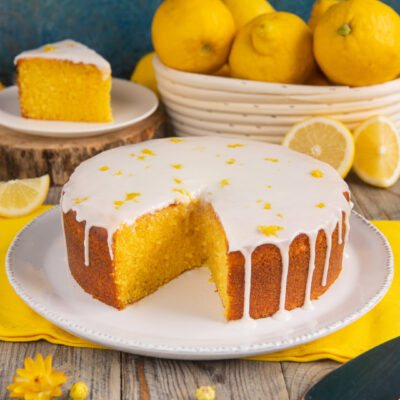 Torta al limone con glassa bianca colante e scorza grattugiata, una fetta già tagliata mostra l'interno soffice