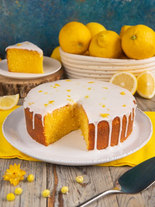 Torta al limone con glassa bianca colante e scorza grattugiata, una fetta già tagliata mostra l'interno soffice