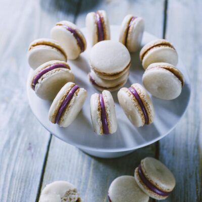 Macaron al lampone con guscio chiaro e farcitura viola, uno morso a rivelare il ripieno