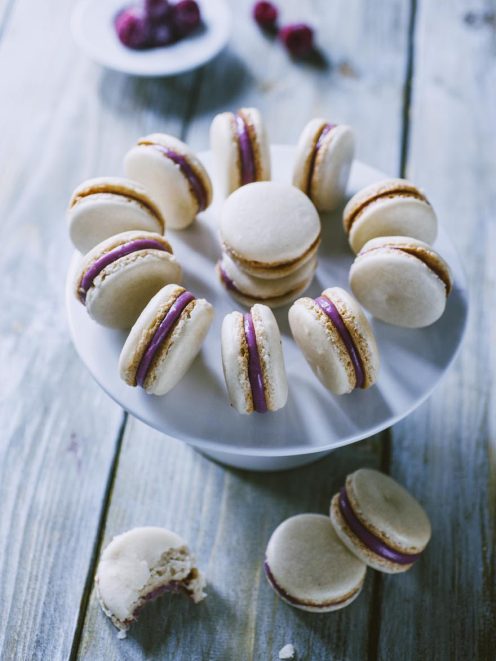 Macaron al lampone con guscio chiaro e farcitura viola, uno morso a rivelare il ripieno