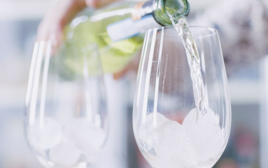 Vino bianco versato da una bottiglia in un calice colmo di ghiaccio