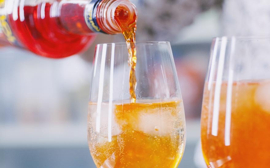 Aperitivo ambrato versato su ghiaccio in un calice già mezzo pieno
