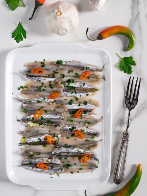 Alici marinate disposte a strati, condite con prezzemolo tritato e rondelle di peperoncino