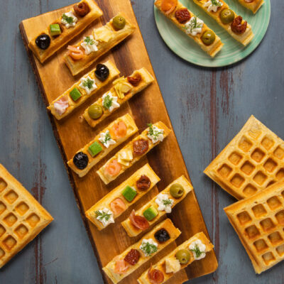 Waffle salati a striscia guarniti con salmone, olive, pomodori secchi e crema su tagliere