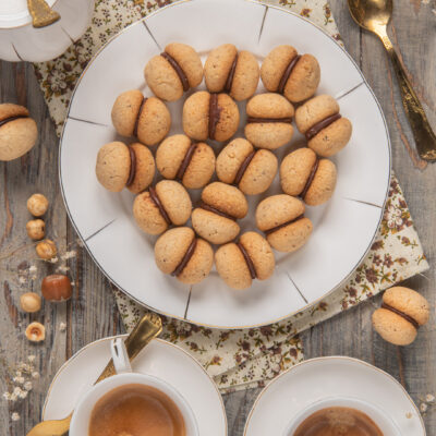 Baci di dama alle nocciole farciti con crema al cioccolato, disposti su un vassoio
