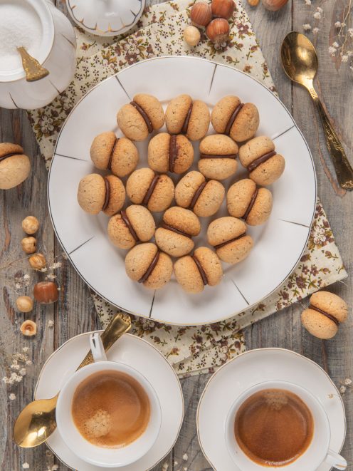 Baci di dama alle nocciole farciti con crema al cioccolato, disposti su un vassoio