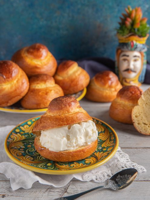 Brioscia col tuppo farcita di gelato alla panna con altre brioches sullo sfondo