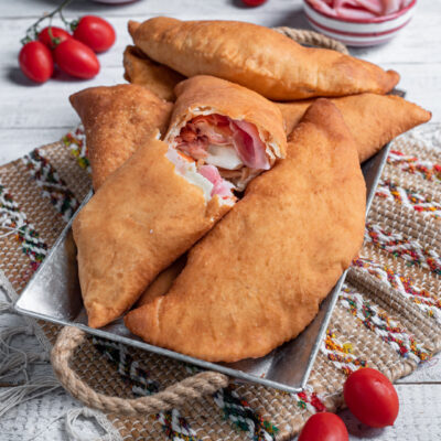 Calzone fritto siciliano dorato, farcito con prosciutto e mozzarella filante tagliato a metà