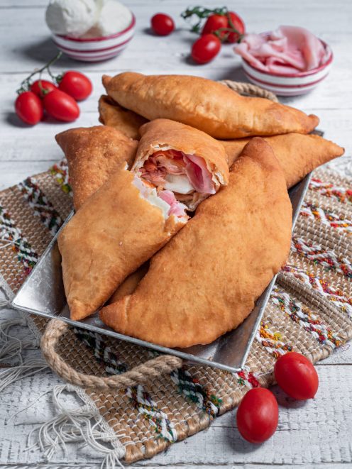 Calzone fritto siciliano dorato, farcito con prosciutto e mozzarella filante tagliato a metà
