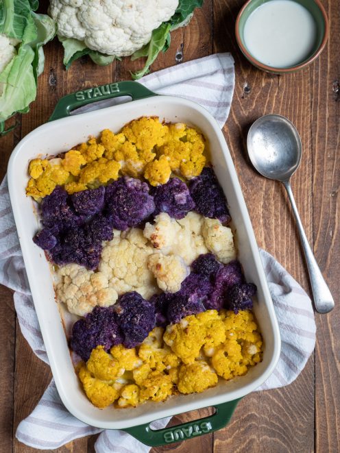 Cavolfiori al forno bianchi, viola e gialli disposti a fasce in teglia con gratin dorato