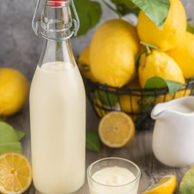 Crema di limoncello in bottiglia e bicchierino, con limoni freschi attorno