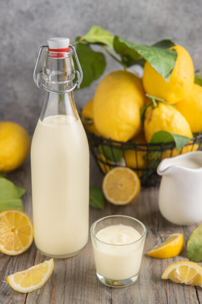 Crema di limoncello in bottiglia e bicchierino, con limoni freschi attorno