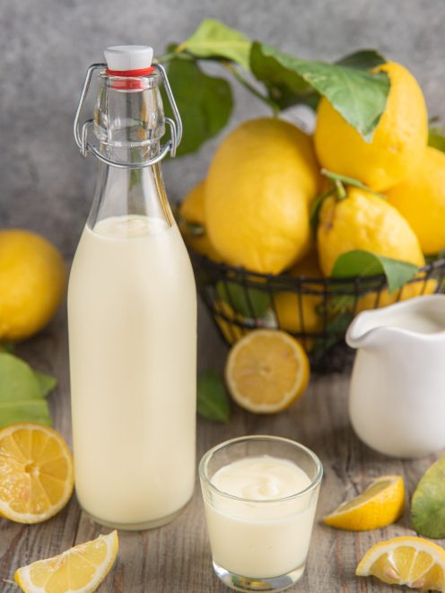 Crema di limoncello in bottiglia e bicchierino, con limoni freschi attorno