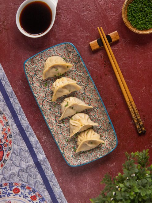 Dumpling disposti in fila e guarniti con erba cipollina tritata