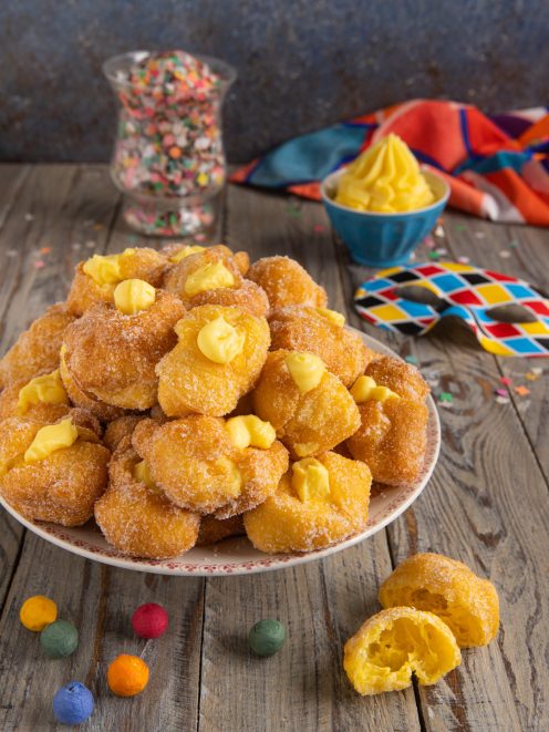 Frittelle di Carnevale ripiene di crema pasticcera, impanate nello zucchero e impilate in abbondanza