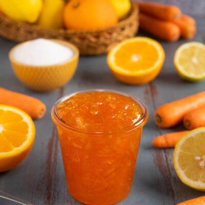 Marmellata di arance, carote e limoni in vasetto con cucchiaino e frutta fresca a fianco
