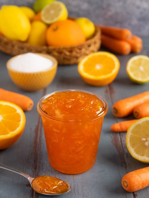 Marmellata di arance, carote e limoni in vasetto con cucchiaino e frutta fresca a fianco