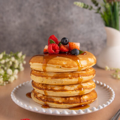 Pancake senza uova impilati con sciroppo d'acero, lamponi, mirtilli e fragole