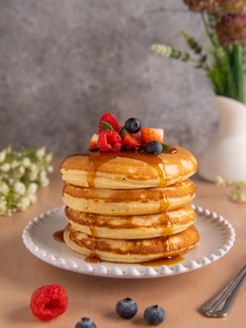 Pancake senza uova impilati con sciroppo d'acero, lamponi, mirtilli e fragole