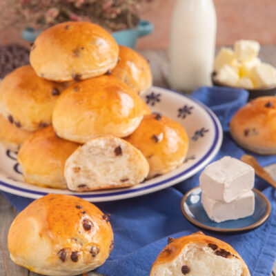 Panini al latte con gocce di cioccolato impilati su un piatto, uno aperto a mostrare la mollica soffice
