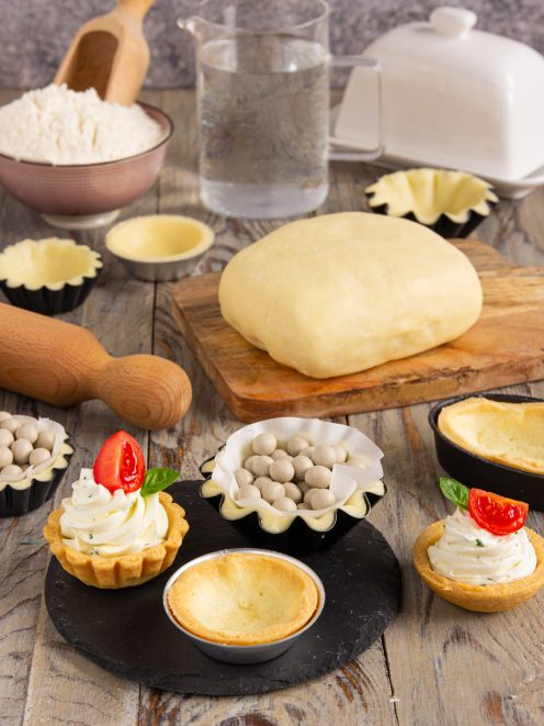 Pasta brisé lavorata in panetto, stampini foderati con pesi di ceramica e tartellette farcite di crema e pomodoro