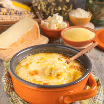 Polenta concia gratinata con crosticina dorata, servita con un cucchiaio di legno