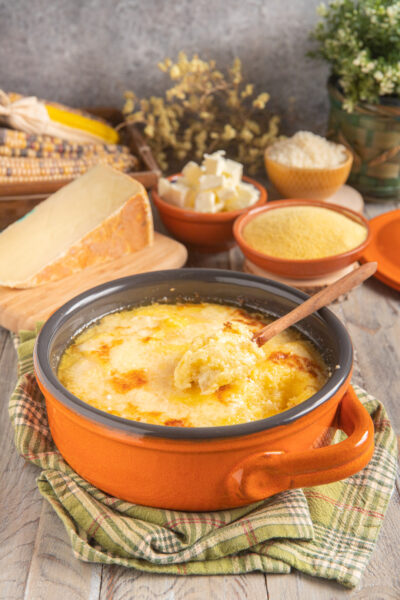 Polenta concia gratinata con crosticina dorata, servita con un cucchiaio di legno