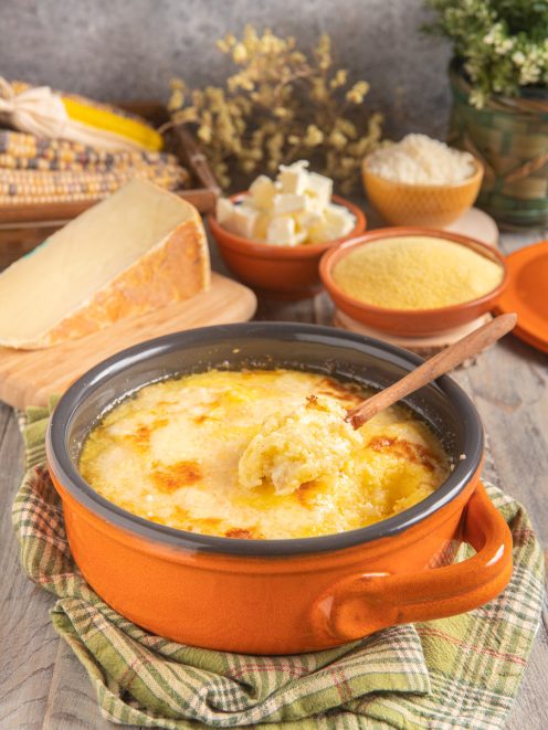 Polenta concia gratinata con crosticina dorata, servita con un cucchiaio di legno
